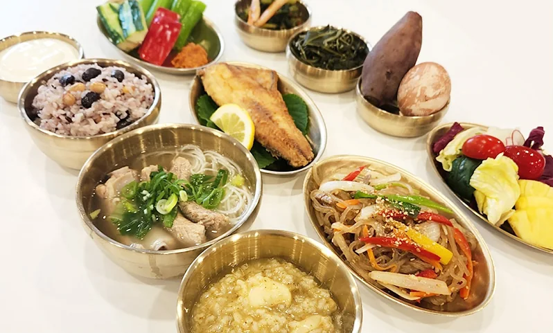 유기 그릇에 담은 한상 차림 — 잡곡밥, 생선구이, 잡채, 국, 죽, 고구마, 과일