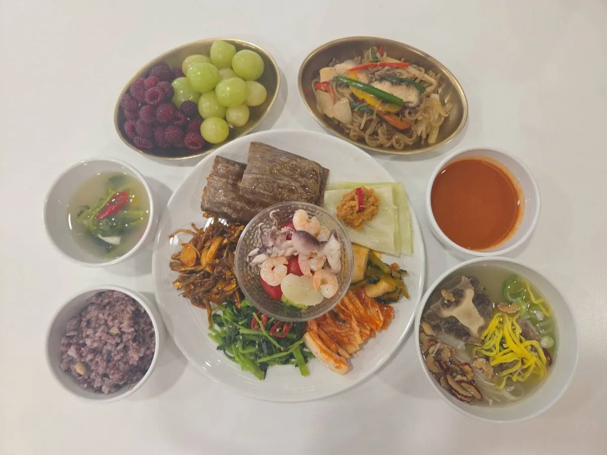 식단 구성 — 흑미 잡곡밥, 구운 고기, 오징어·새우 냉채, 양배추쌈과 쌈장, 볶은 나물, 시금치나물, 배추김치, 잡채, 국물 요리, 토마토 주스, 청포도·라즈베리